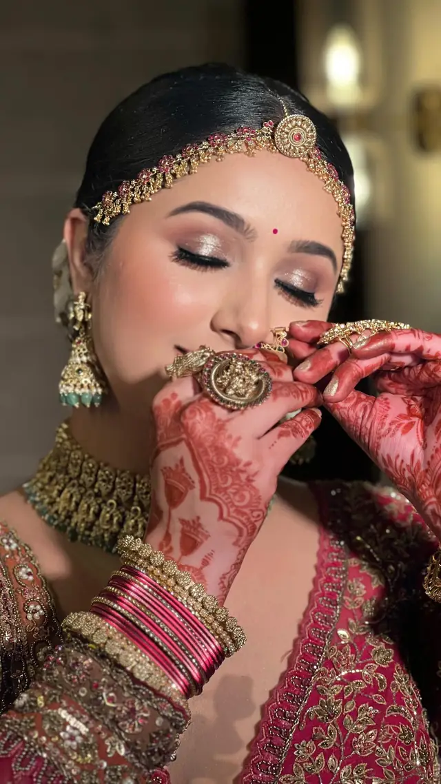 A bride with her eyes closed, a gold headpiece with a green stone, kundan and green-stone earrings and necklace, a green sari-drape blouse.